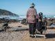 woman standing beside woman on white wooden chair facing body of water