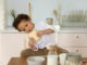 A young boy sits in a cozy kitchen enjoying a slice of bread, surrounded by breakfast items.