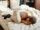 A young woman sleeps peacefully in a fetal position on a bed, surrounded by soft pillows and warm blankets.