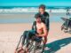man in black shorts sitting on black wheelchair on beach during daytime